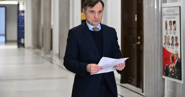 Mężczyzna w garniturze trzyma dokumenty, być może związane z aferą z Funduszem Sprawiedliwości u Ziobry i PiS.