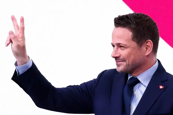 Rafał Trzaskowski pokazuje dwa palce, symbolizując zwycięstwo.